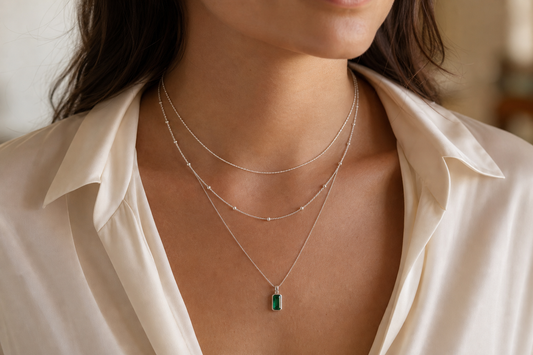 Three well-spaced silver necklaces layered with a green emerald pendant
