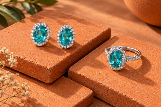 Blue-green halo earrings and an oval ring on offset orange tiles.